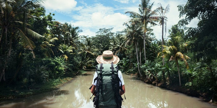 Traveling woman with a large backpack in a tropical river blue sky and white clouds