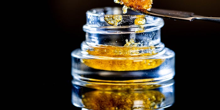 Live Resin in a glass container. An orange sticky substance that looks like salmon row is scooped up with a spoon.