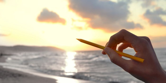 Artist with a pencil in hand is getting creative inspiration to draw from the ocean scenery.