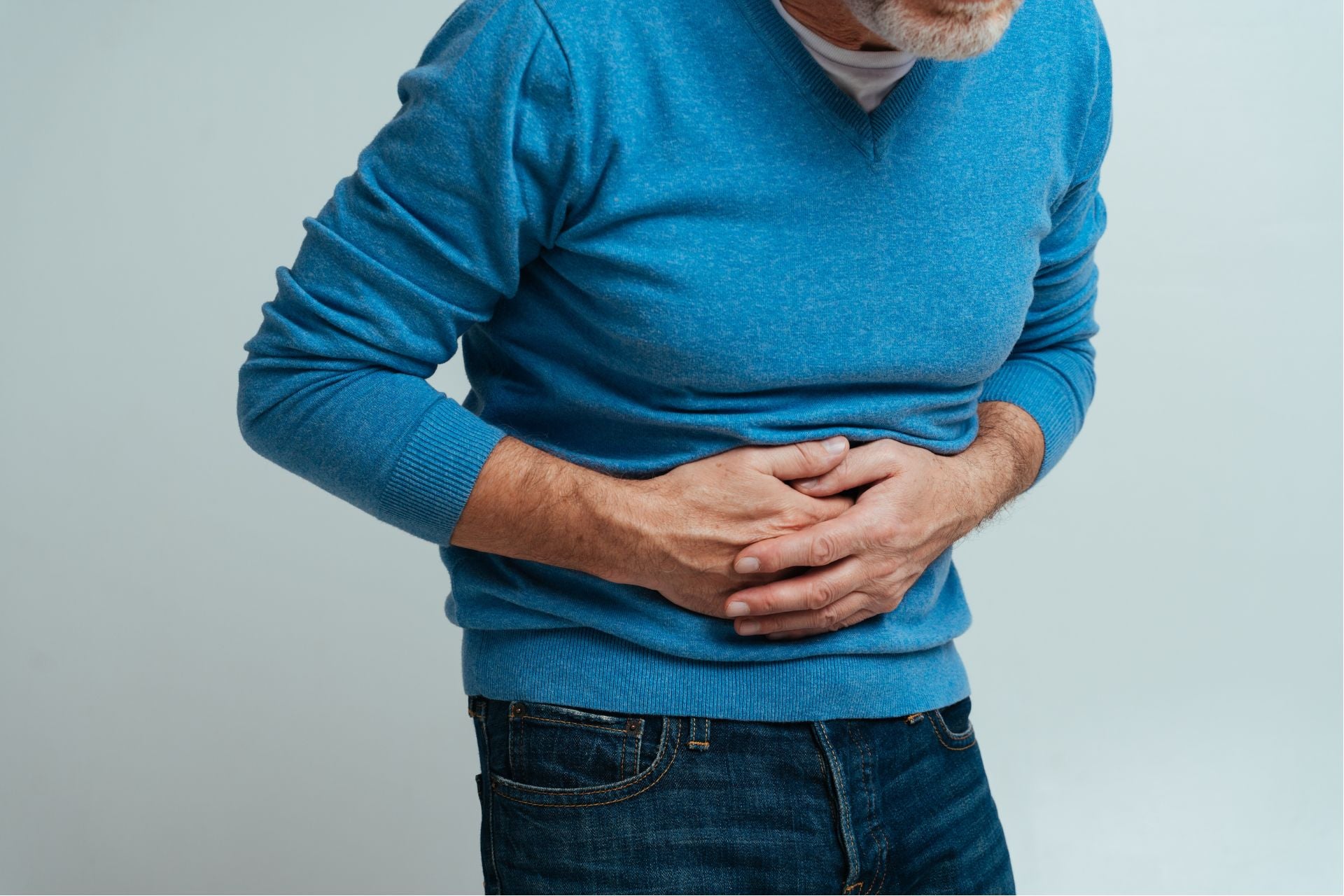 Elderly man suffering from IBD disease. He is holding his stomach with both hands.