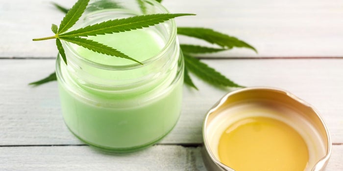 Cannabis topical cream in a glass jar on a white wooden bench.