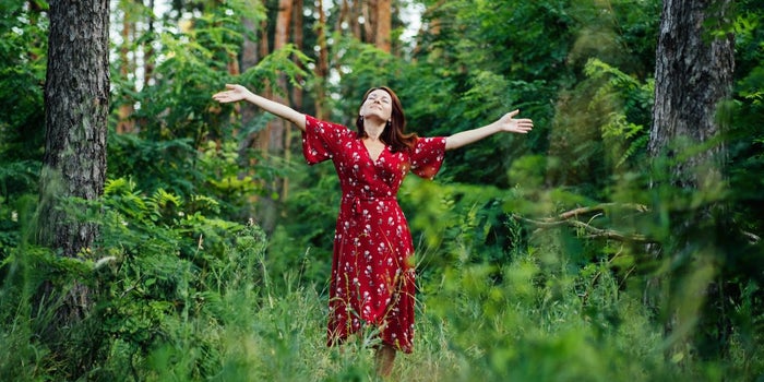 A young woman standing in nature with her arms spread out.